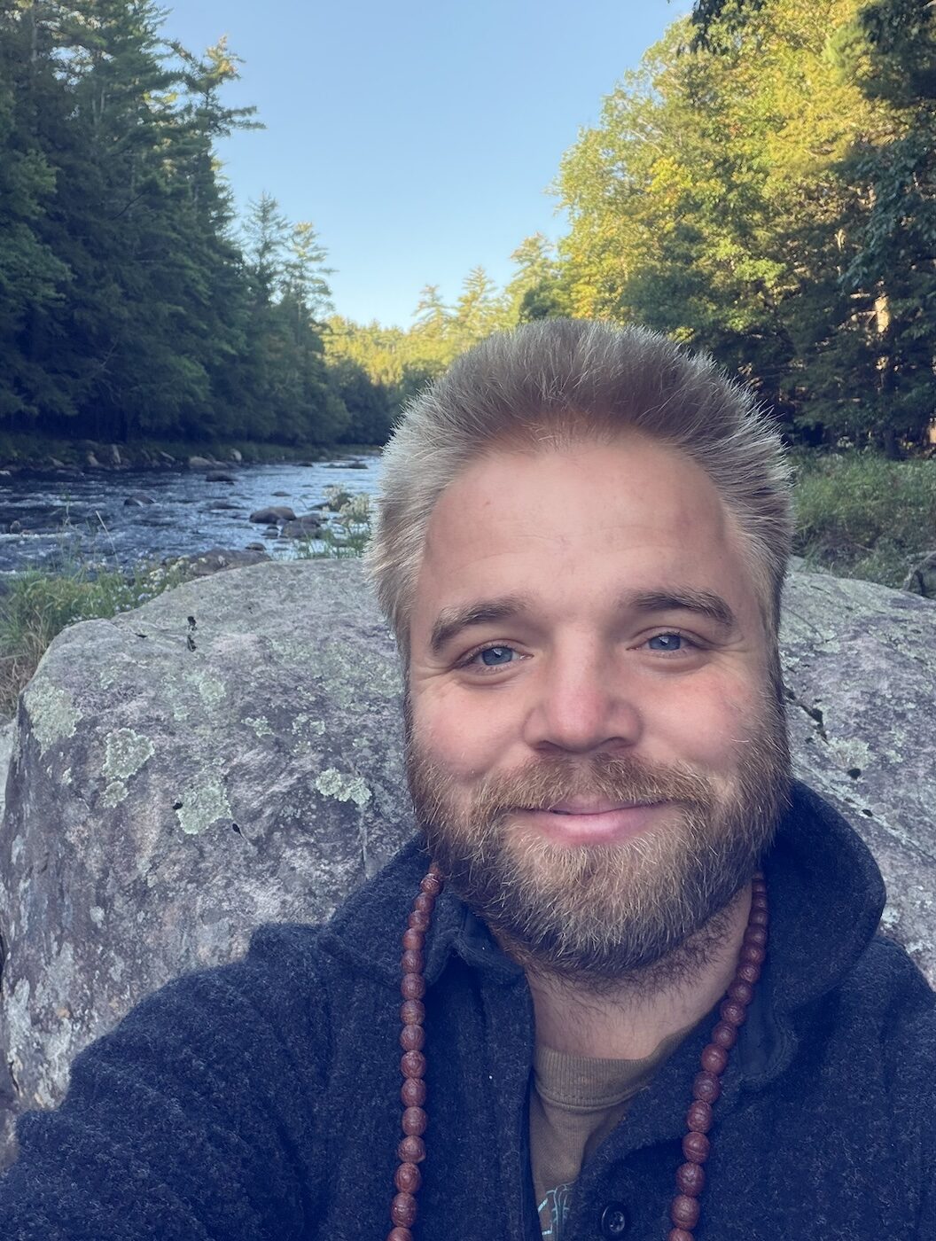 Davis Trachte smiling outdoors beside a forest river
