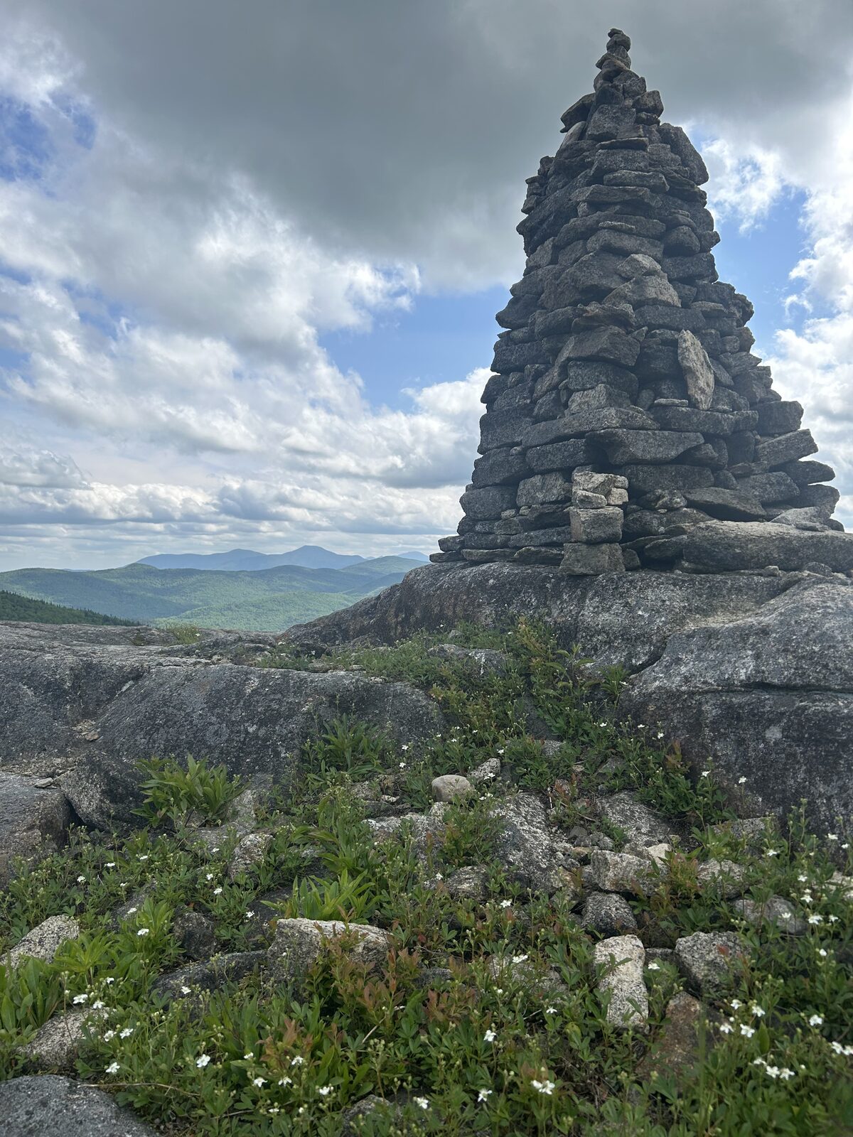 A cairn atop an Adirondack summit, overlooking forested peaks